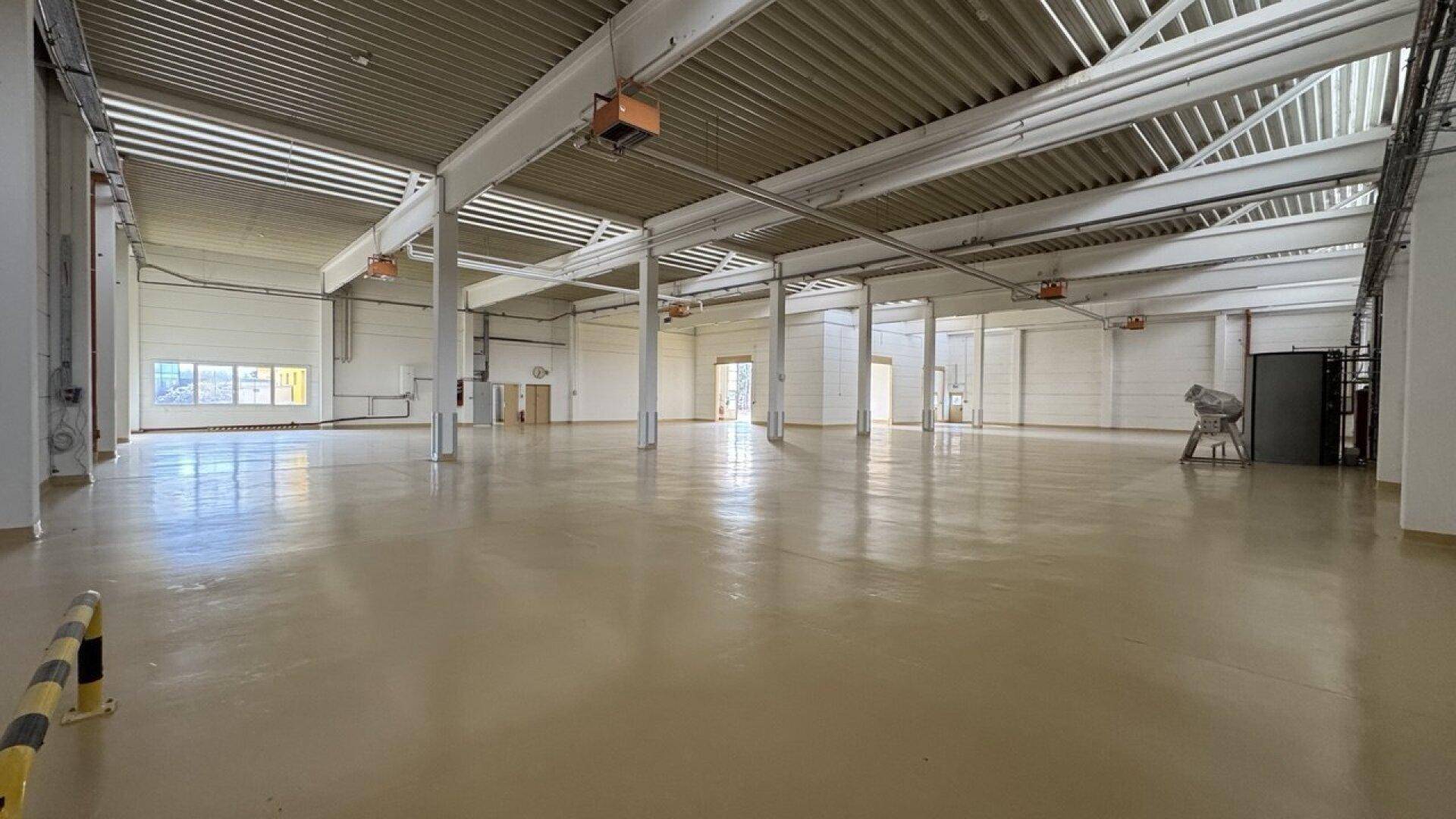 Weitläufige Lagerhalle mit hohen Decken, sichtbaren Stahlträgern und einem glänzenden Industrieboden.