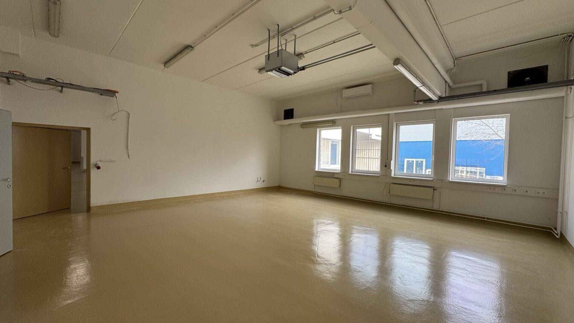 Helles Büro mit mehreren Fenstern, abgehängter Decke und einem Projektor an der Decke.