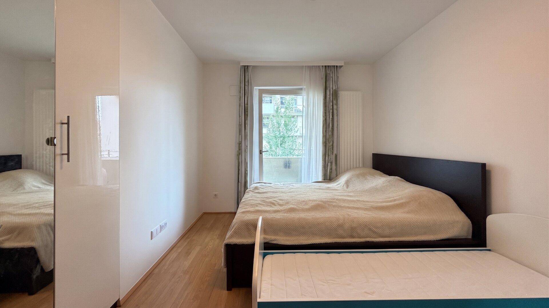 Schlafzimmer mit Doppelbett, Holzboden und Zugang zu einem französischen Balkon.
