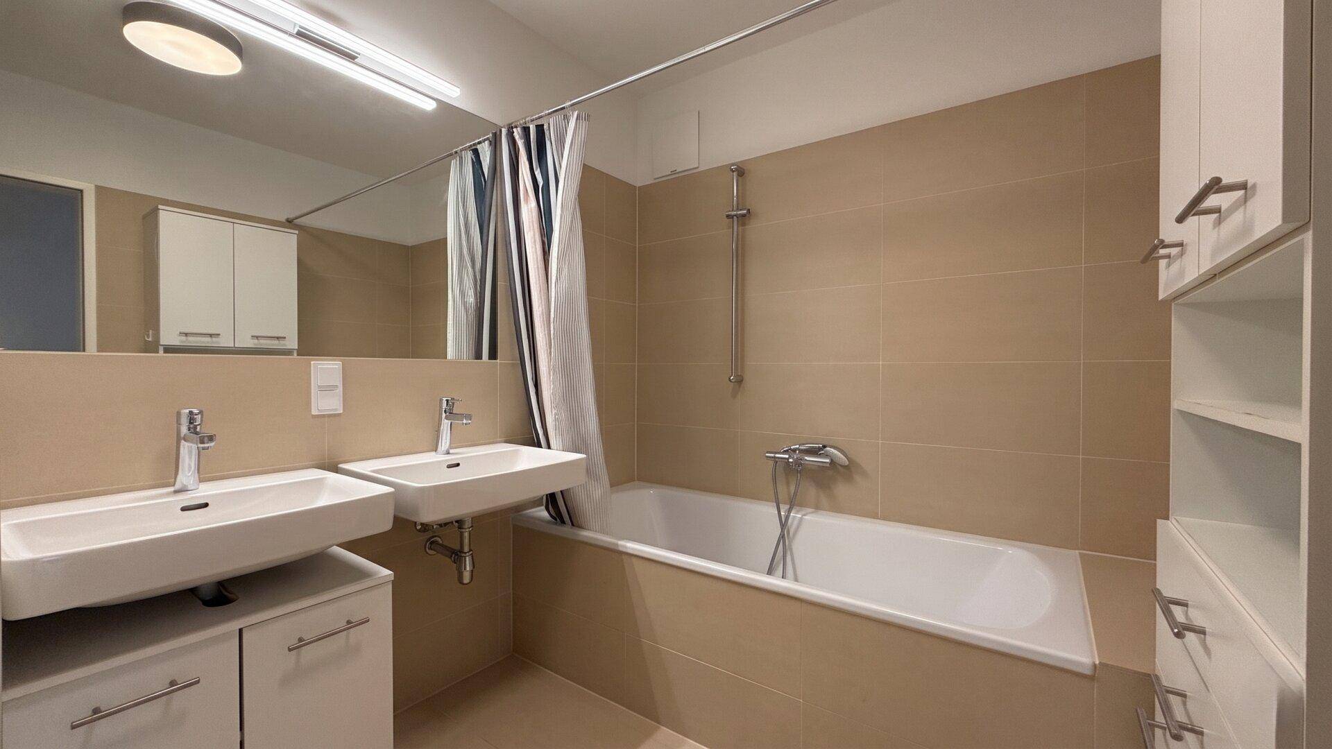 Modernes Badezimmer mit Doppelwaschbecken, Badewanne und beigefarbenen Fliesen.