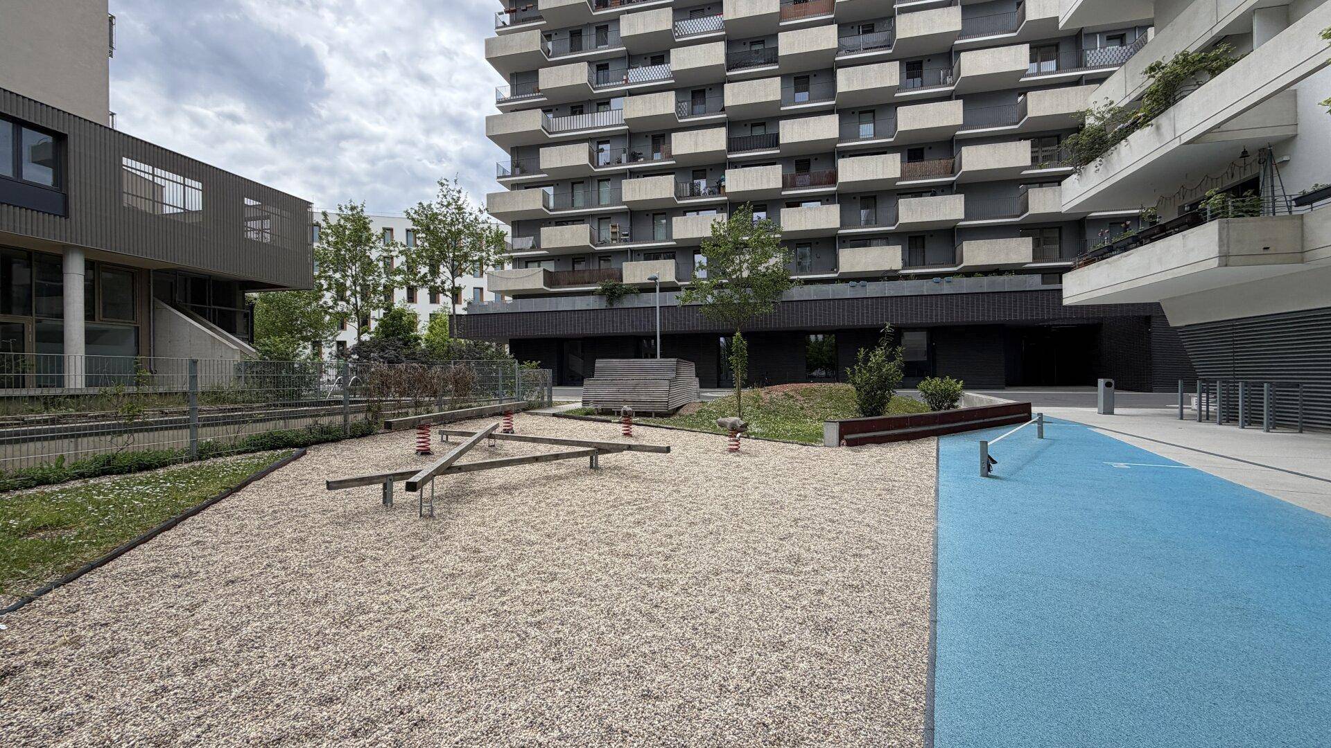 Außenbereich eines Wohnkomplexes mit Spielplatz und modernen Gebäuden im Hintergrund.