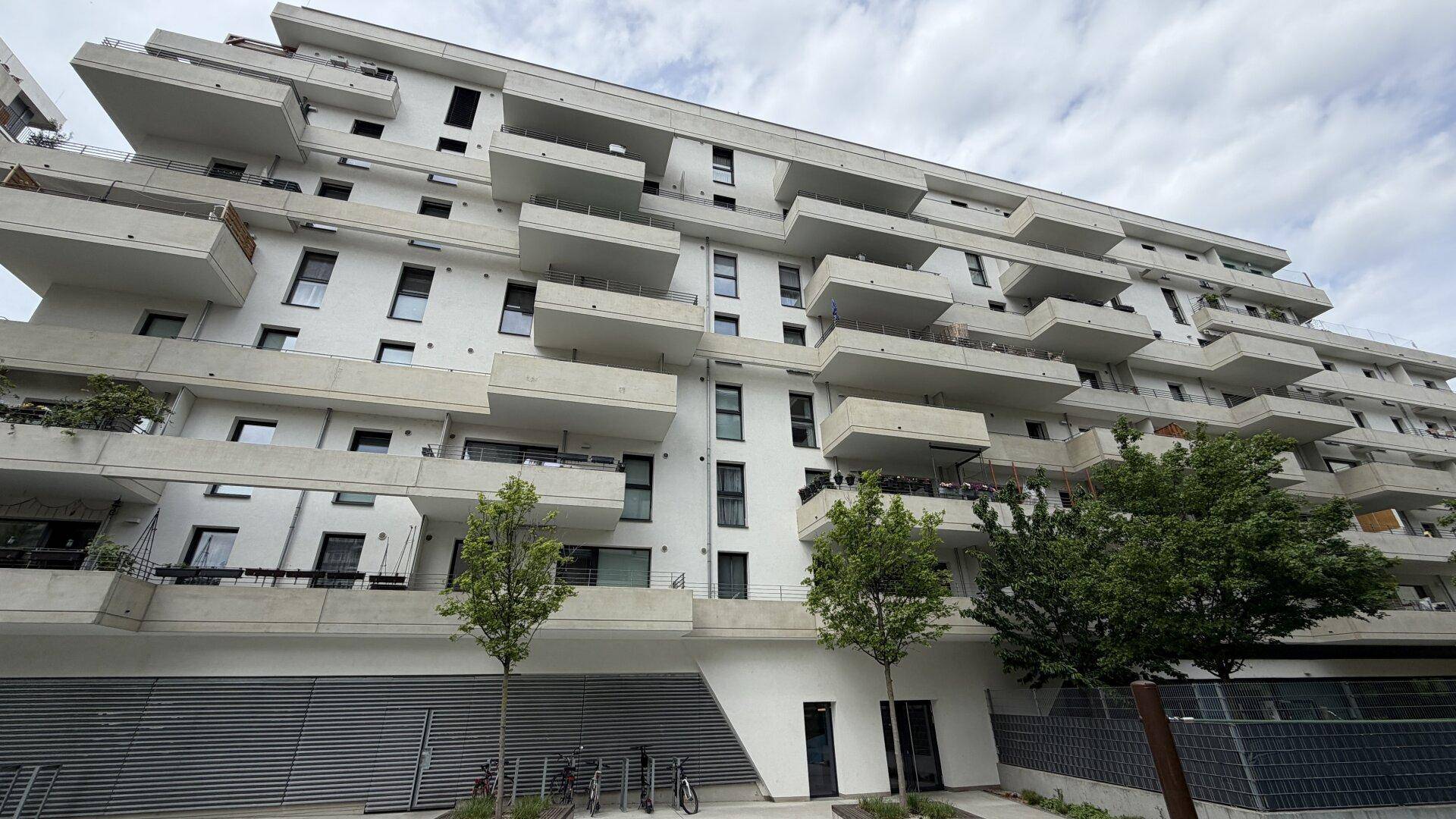 Moderne Wohnanlage mit vielen Balkonen und einer hellen Fassade unter bewölktem Himmel.