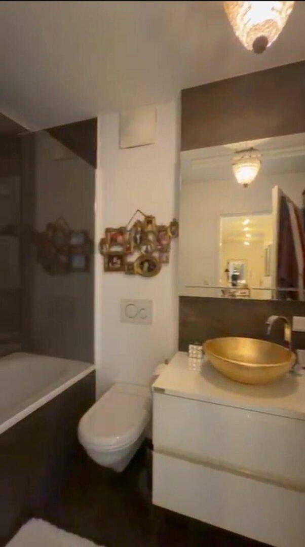 Modernes Badezimmer mit goldener Waschschale, Wand-WC und dekorativen Elementen.