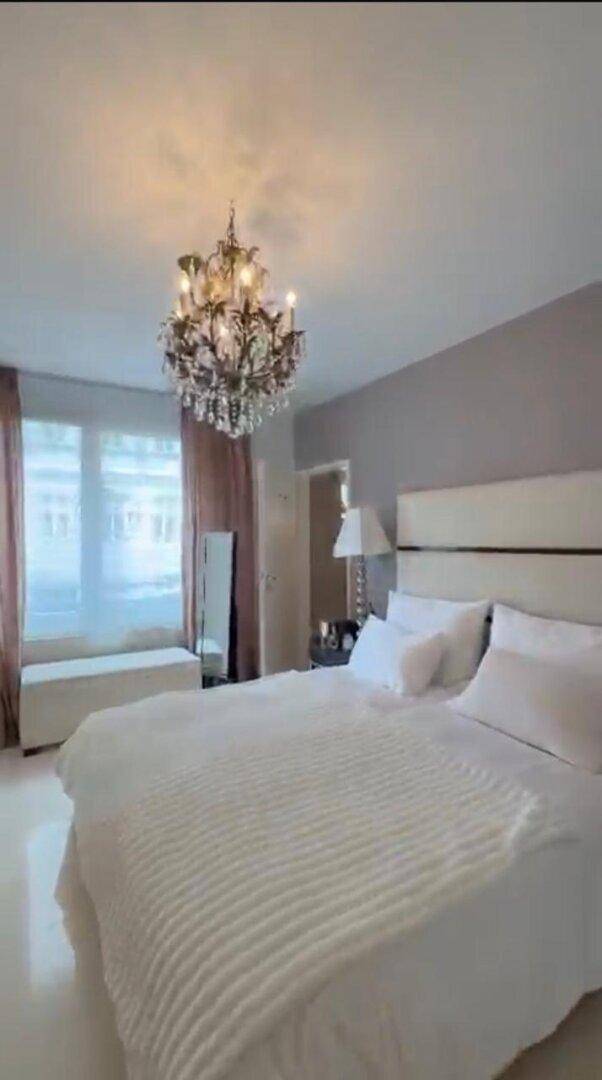 Geräumiges Schlafzimmer mit großem Bett, Kronleuchter und hellen Vorhängen am Fenster.