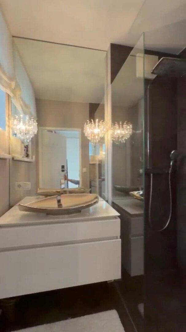 Elegantes Badezimmer mit großem Spiegel, goldener Waschschale und Duschbereich.