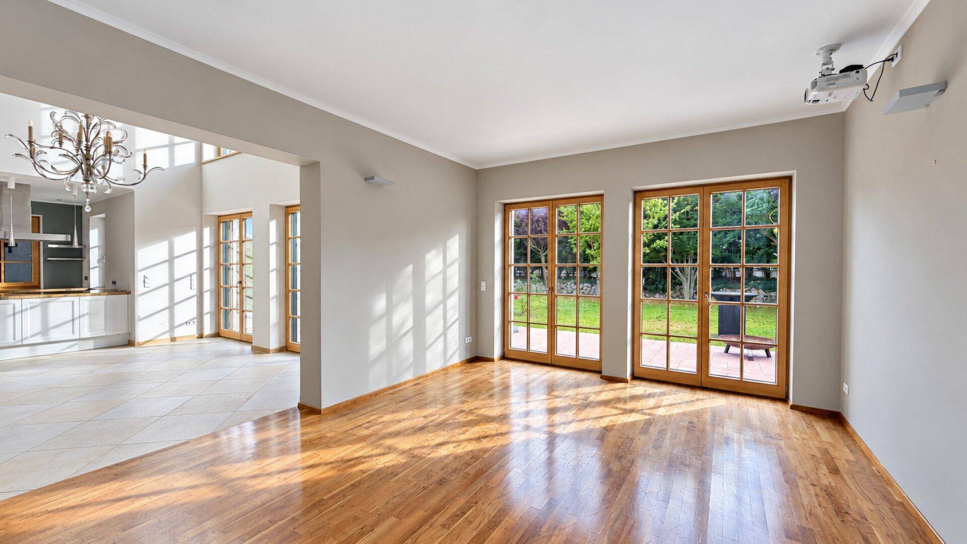 Geräumiges Wohnzimmer mit Holzboden, großen Fenstern und Zugang zum Garten.