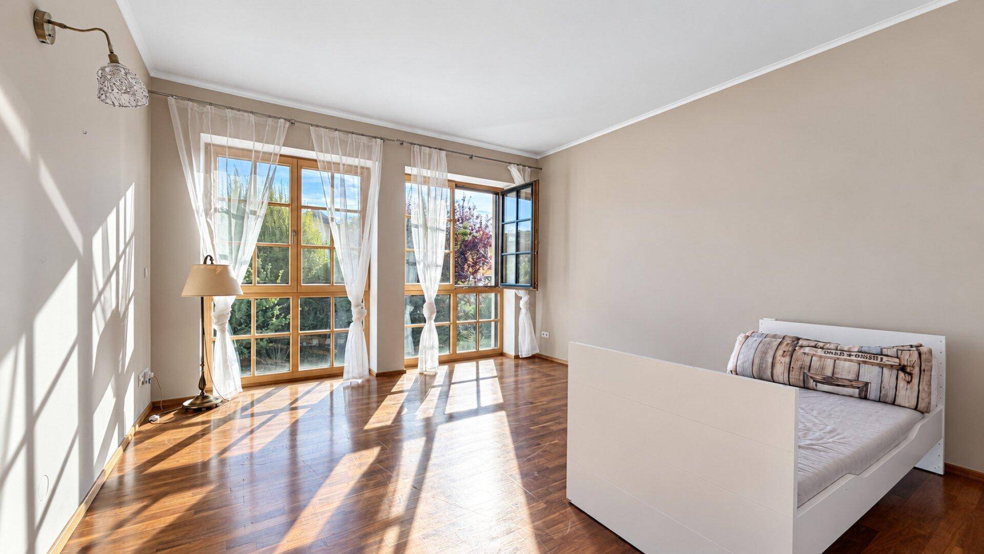 Helles Schlafzimmer mit Holzboden, großen Fenstern und Vorhängen.