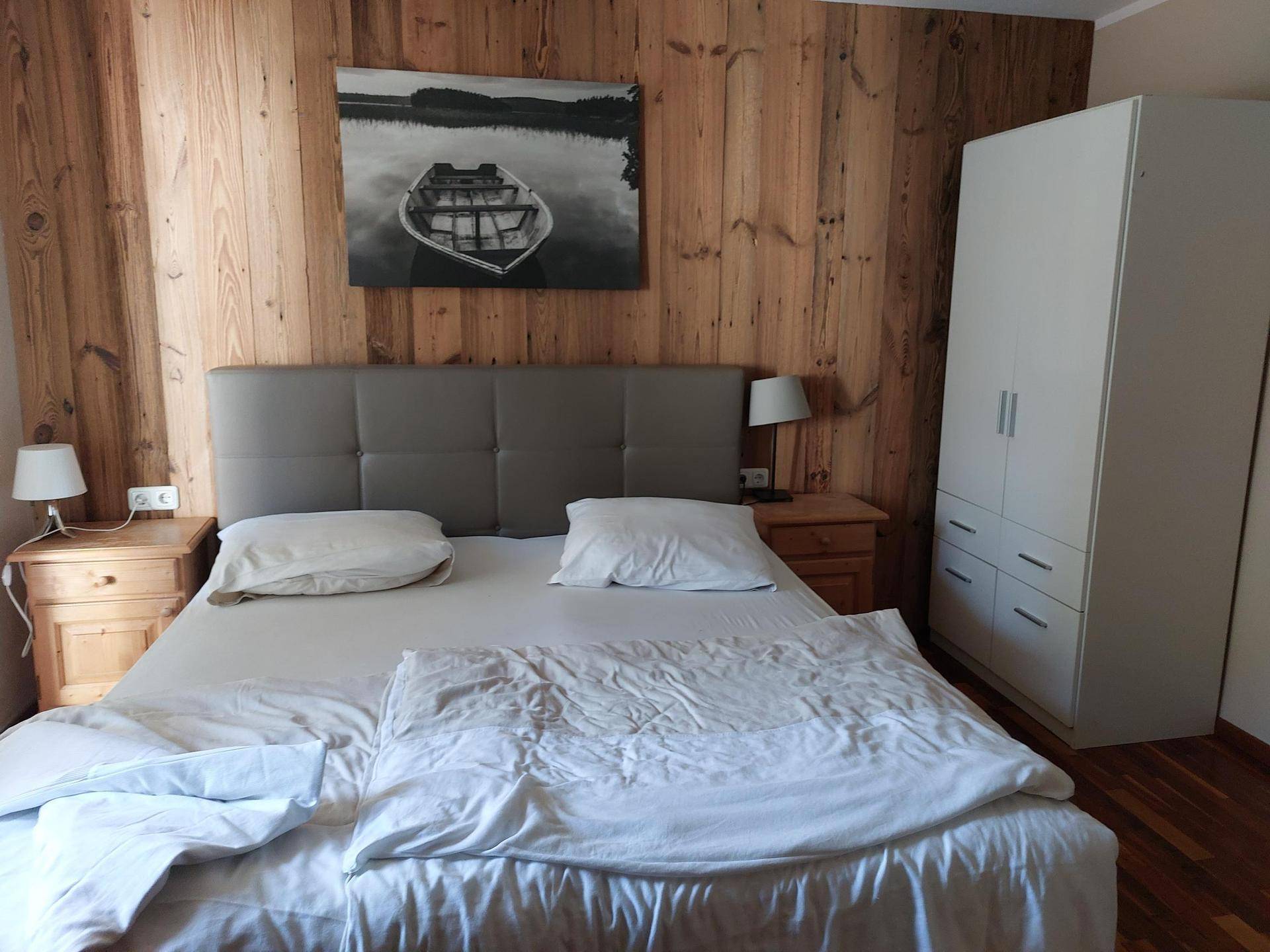 Geräumiges Schlafzimmer mit Doppelbett, Holzwand und weißem Kleiderschrank.