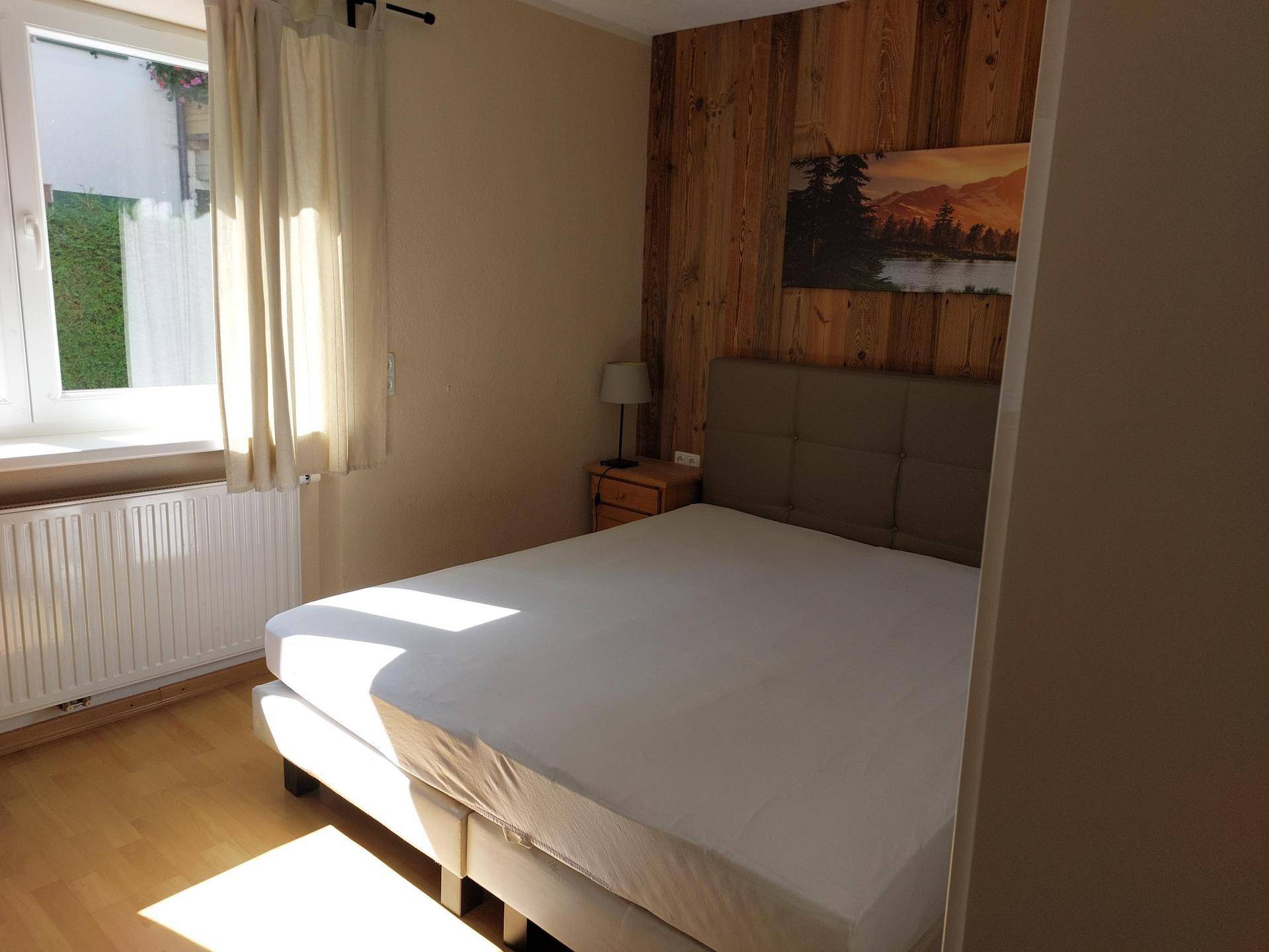 Gemütliches Schlafzimmer mit Doppelbett, Holzwand und natürlichem Lichteinfall.