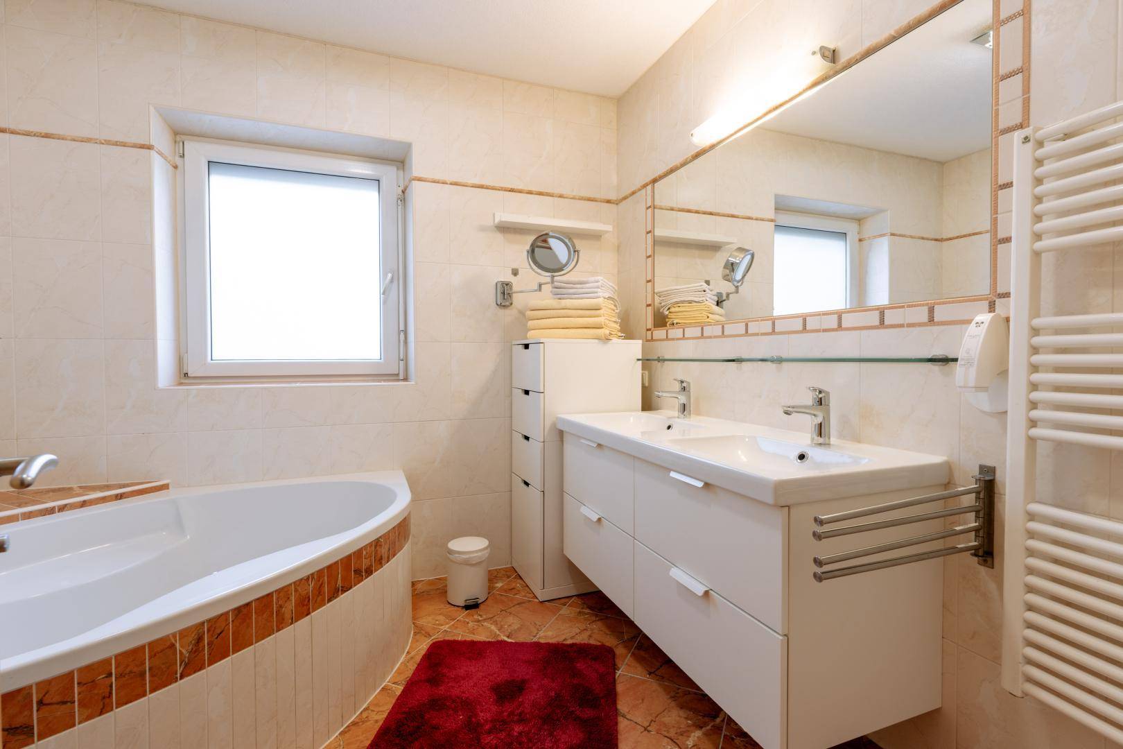 Helles Badezimmer mit Eckbadewanne, Doppelwaschbecken und großem Spiegel.