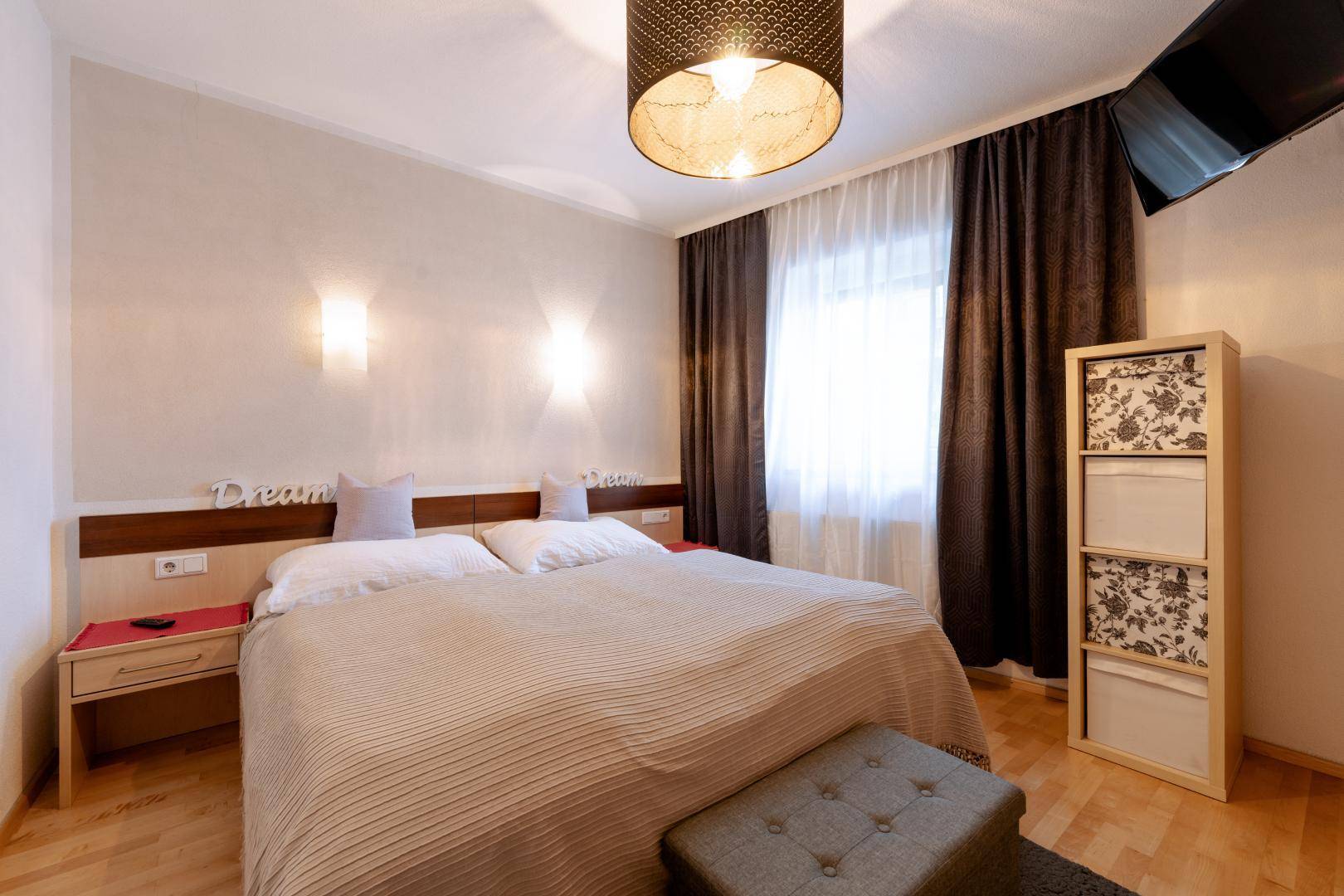 Gemütliches Schlafzimmer mit Doppelbett, Holz-Kopfteil und dunklen Vorhängen.