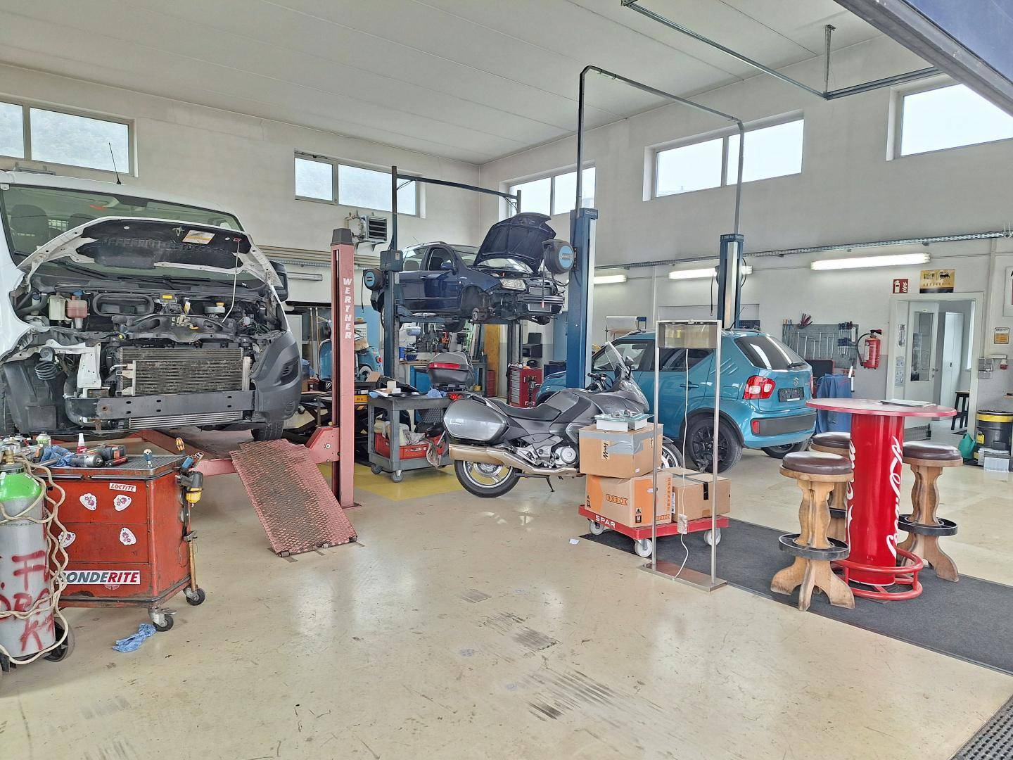Helle und geräumige KFZ-Werkstatt mit mehreren Hebebühnen, Werkzeugen und Fahrzeugen.
