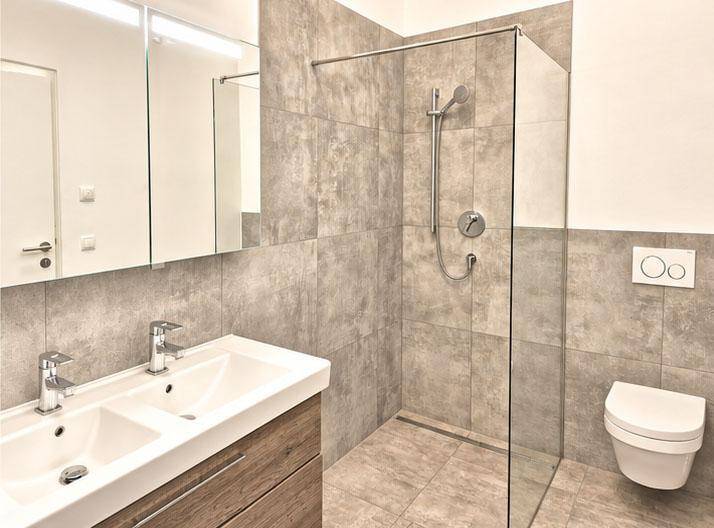 Modernes Badezimmer mit grauen Fliesen, begehbarer Dusche, Doppelwaschbecken und Wand-WC.