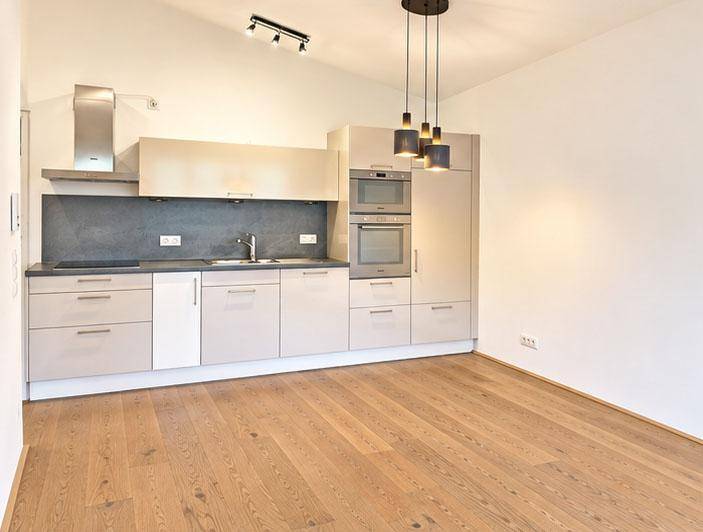 Moderne Einbauküche mit hellgrauen Schränken, integrierten Geräten und Holzboden.