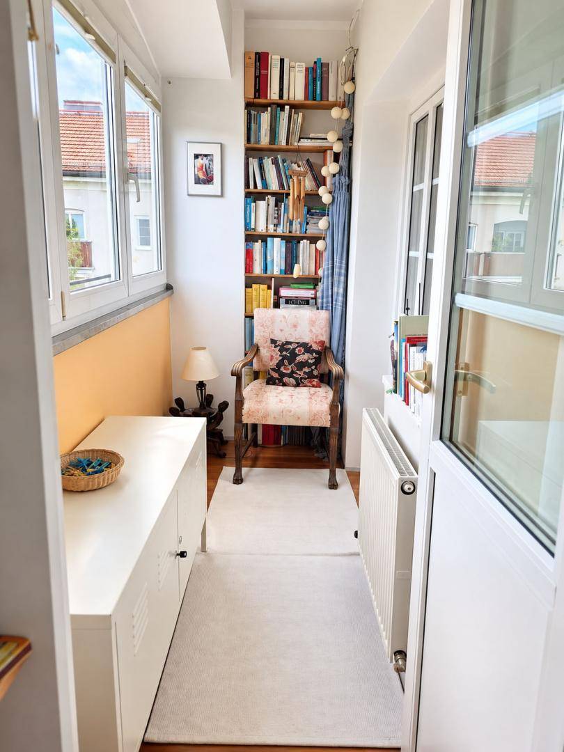 Verglaste Loggia mit Bücherregal, Lesesessel und hellem Holzboden.