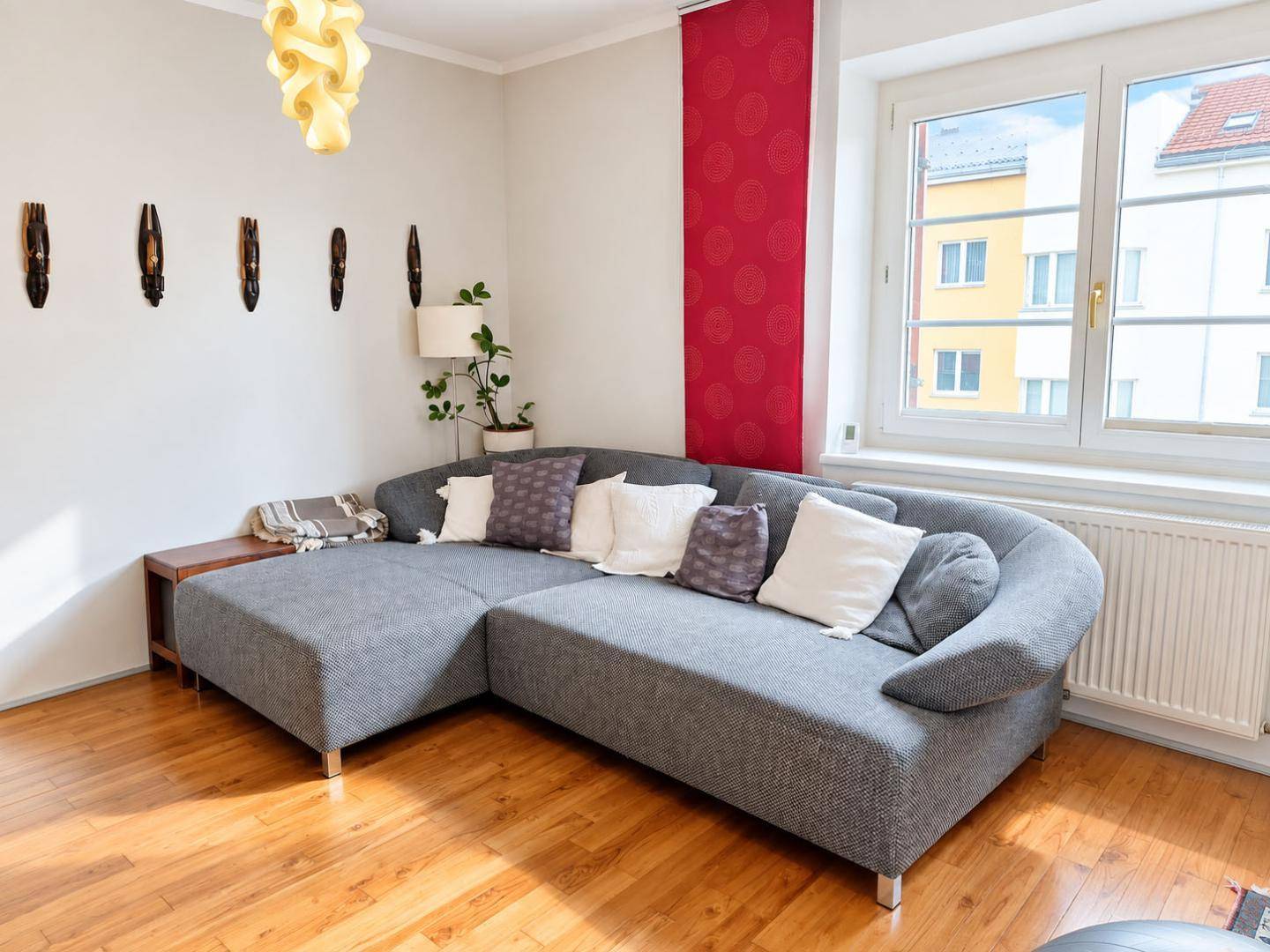 Gemütliches Wohnzimmer mit großem Ecksofa, Holzboden und breitem Fenster.