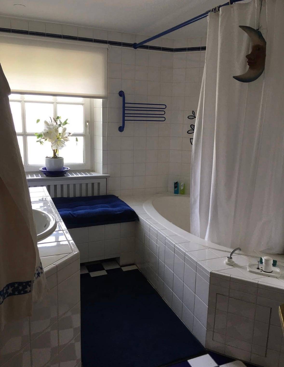 Badezimmer mit Badewanne, Fenster und blauen Akzenten, ausgestattet mit weißen Fliesen.