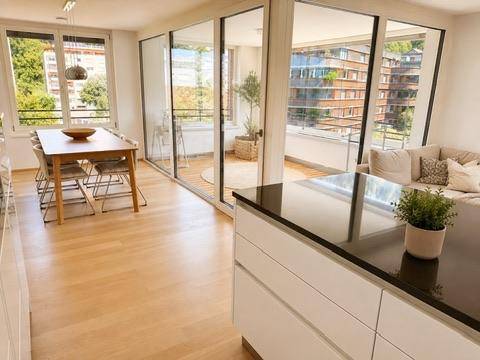 Lichtdurchfluteter Wohn- und Essbereich mit Holzboden und Zugang zu einem Balkon mit Stadtblick.