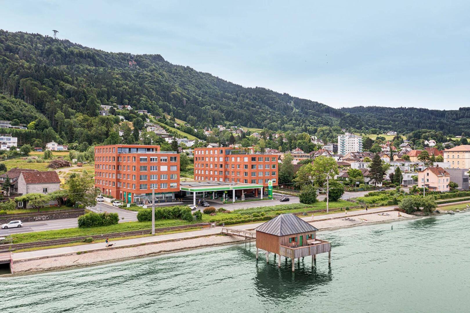 Luftaufnahme einer modernen Wohnanlage am Seeufer mit Bergblick und umliegender Natur.