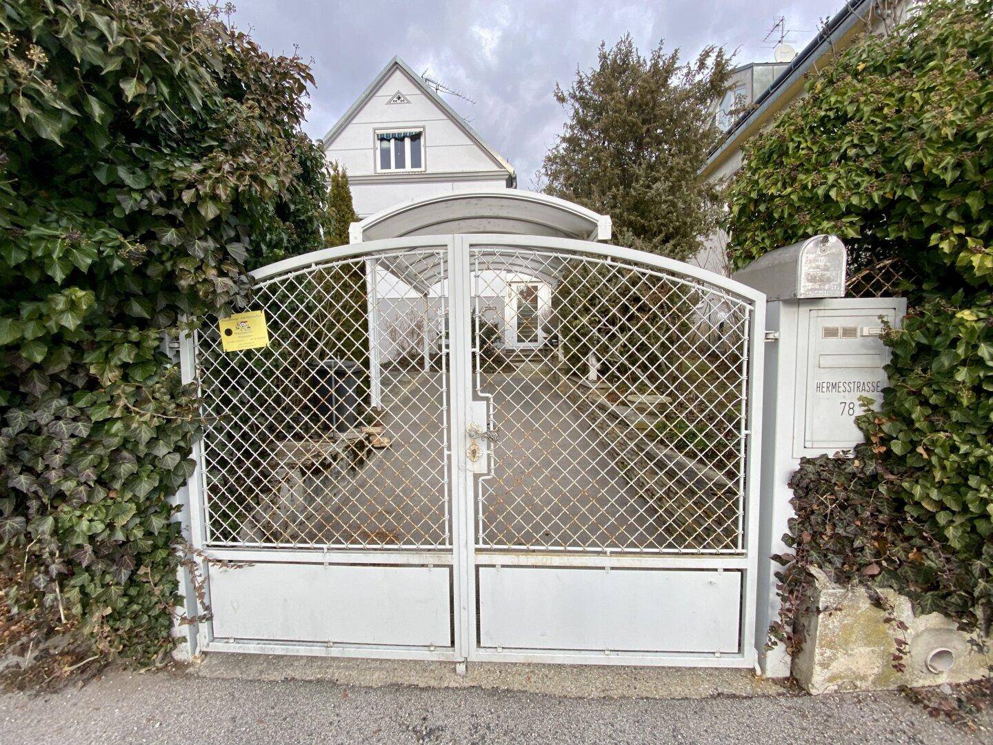 Einfahrtstor zum Grundstück mit Carport und umgebender Bepflanzung.