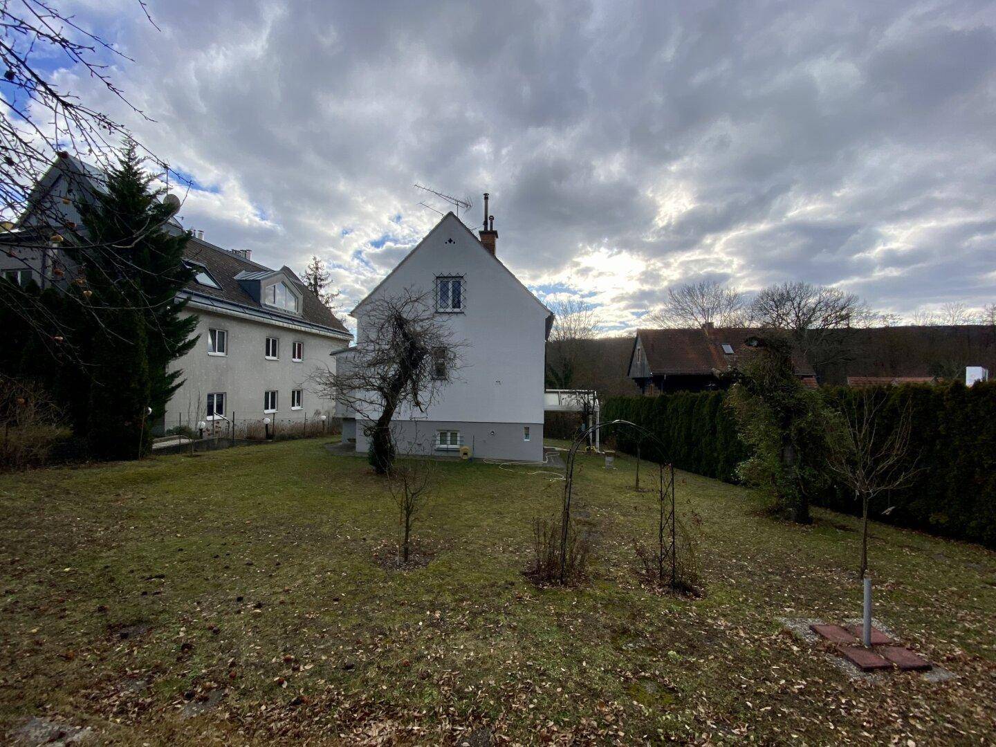 Rückseite des Hauses mit großem Garten und bewölktem Himmel.