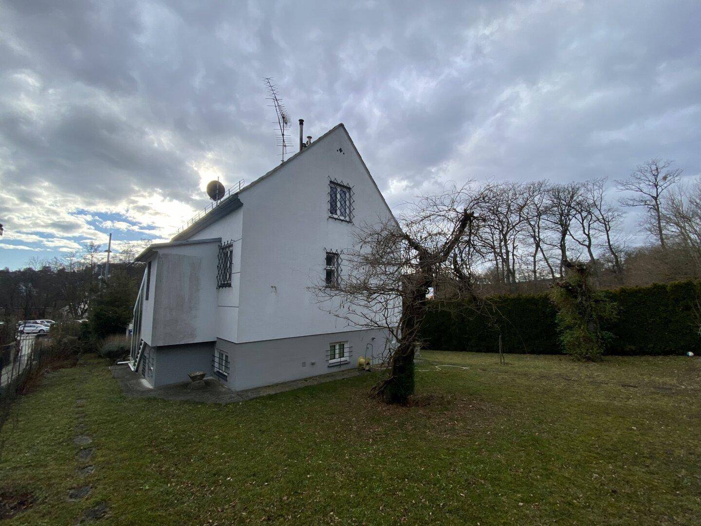 Seitenansicht des Hauses mit Garten und Bäumen unter bewölktem Himmel.