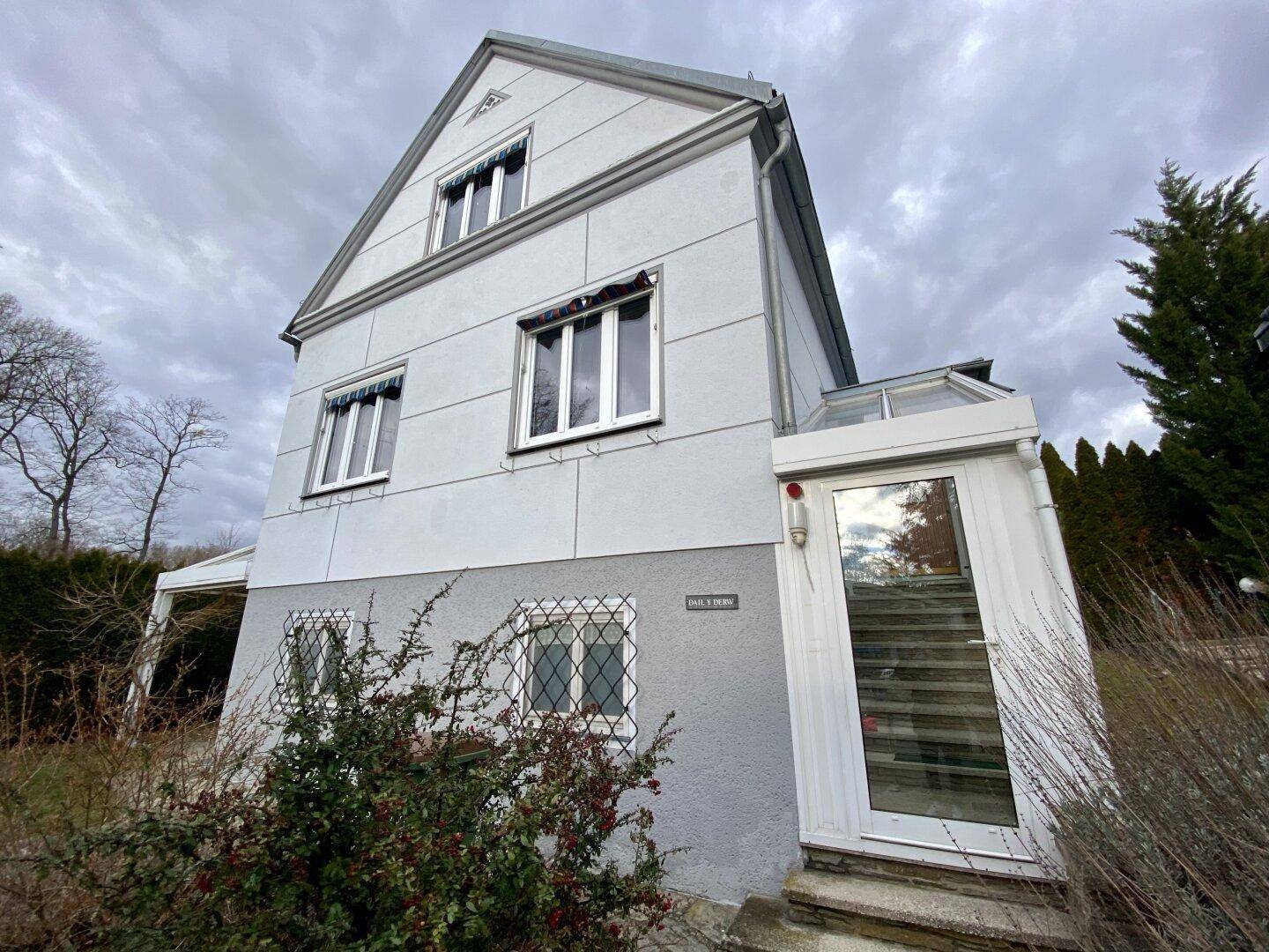 Vorderansicht des Hauses mit Fassade, Fenstern und einem verglasten Anbau.