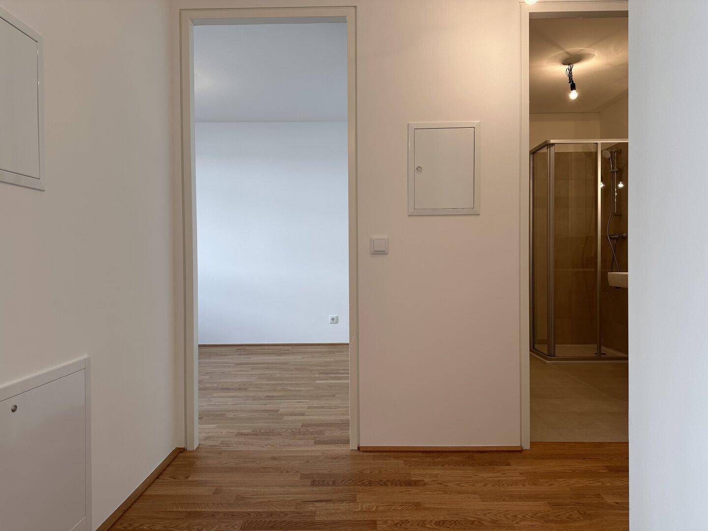 Heller Flur mit Parkettboden, der zu einem Zimmer und einem Badezimmer führt.