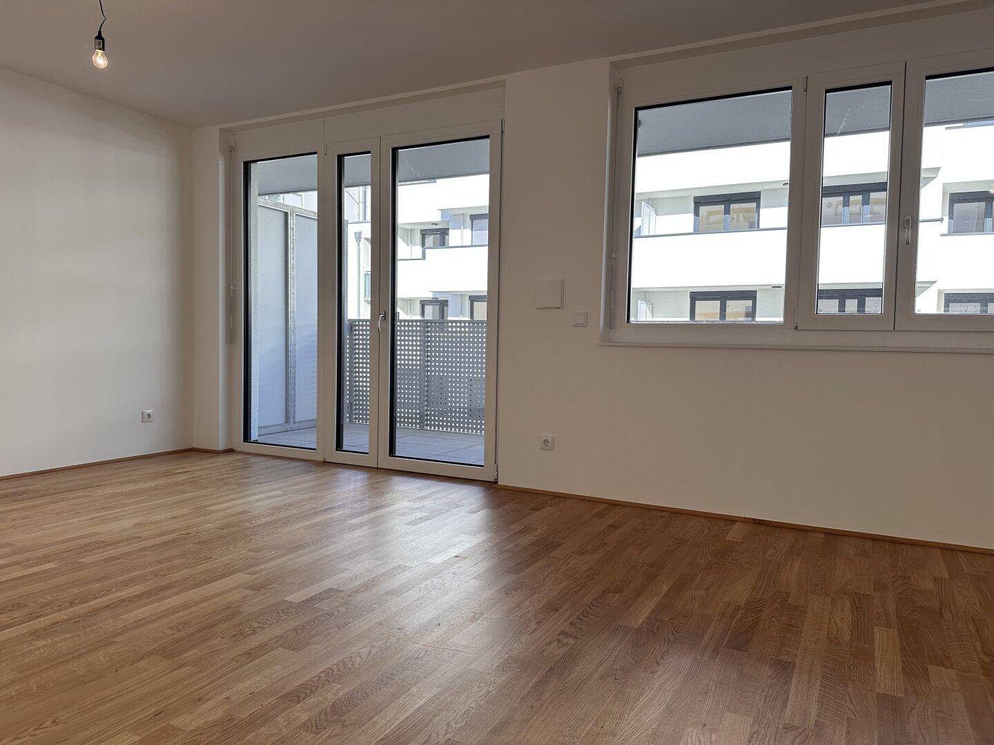 Helles Zimmer mit Parkettboden und breitem Zugang zu einem Balkon.