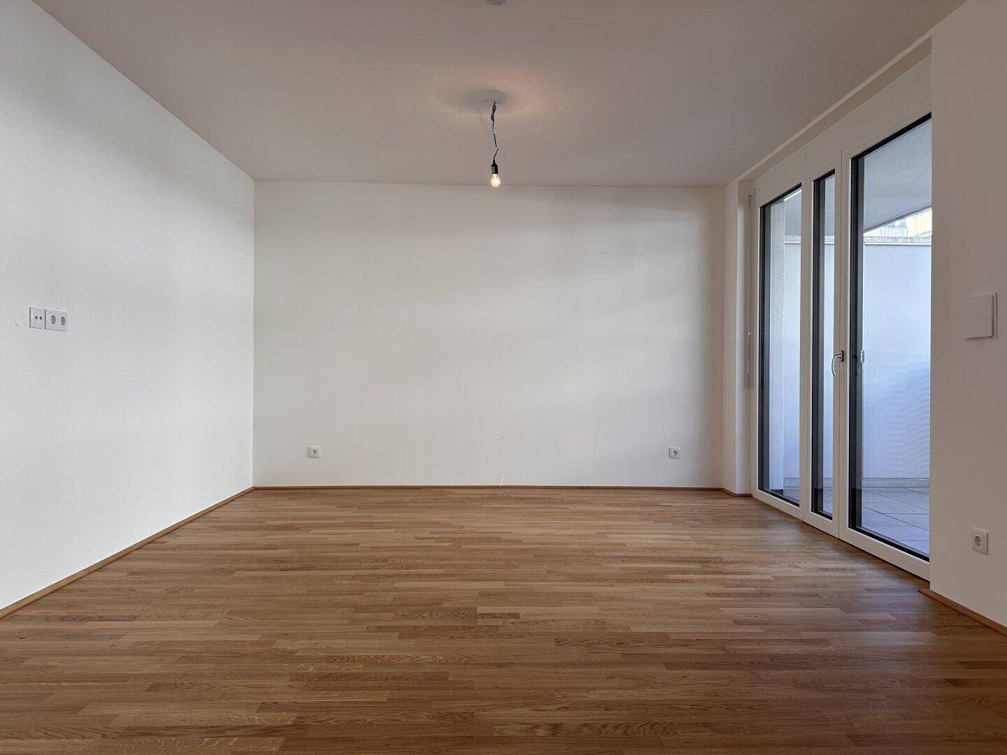 Geräumiges, helles Zimmer mit Parkettboden und Zugang zu einem Außenbereich.