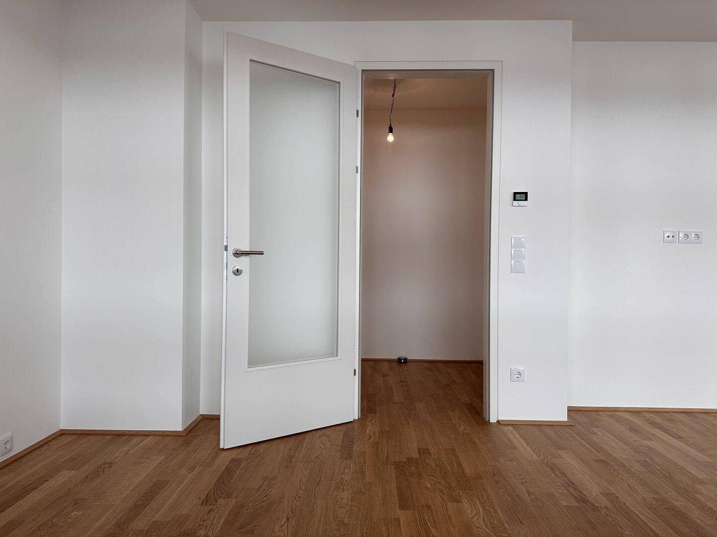 Helles Zimmer mit Parkettboden und einer Tür mit Milchglas-Einsatz.