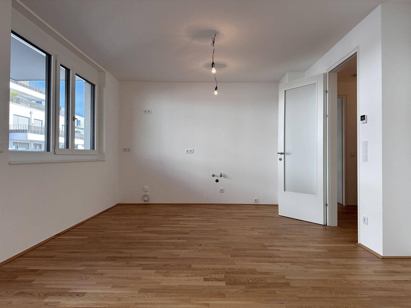 Heller Raum mit Parkettboden und Anschlüssen für eine Küche, bereit zum Einbau.