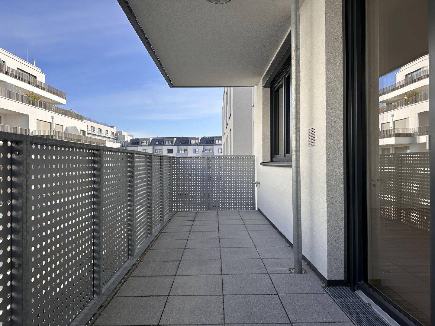 Langer Balkon mit Fliesenboden und perforiertem Metallgeländer, Blick auf die Umgebung.
