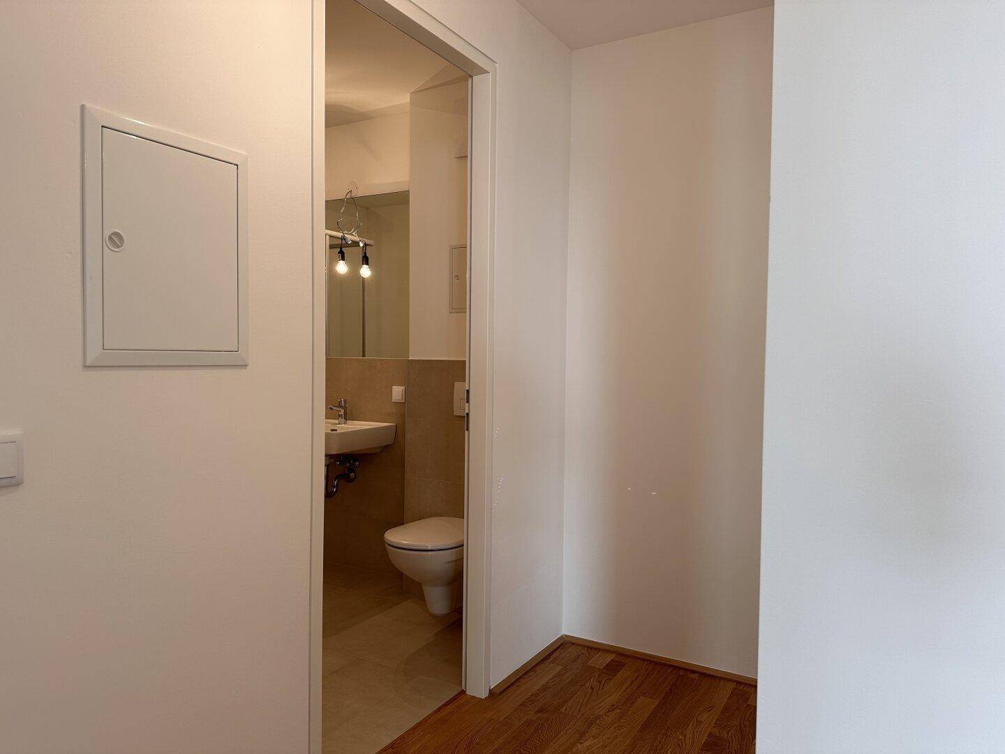 Blick in ein modernes WC mit Wand-WC und Waschbecken, helle Fliesen.