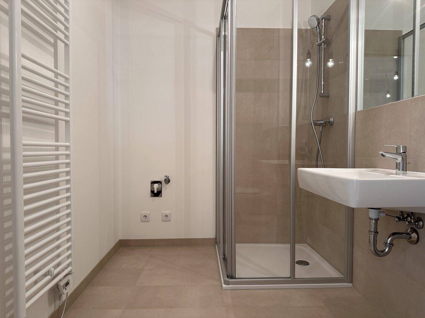 Modernes Badezimmer mit Duschkabine, Waschbecken und Handtuchheizkörper in hellen Farbtönen.