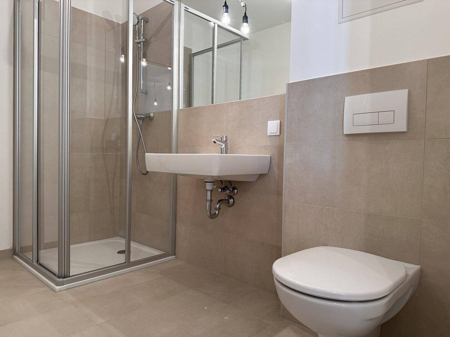 Helles Badezimmer mit Duschkabine, Wand-WC und modernem Waschbecken.