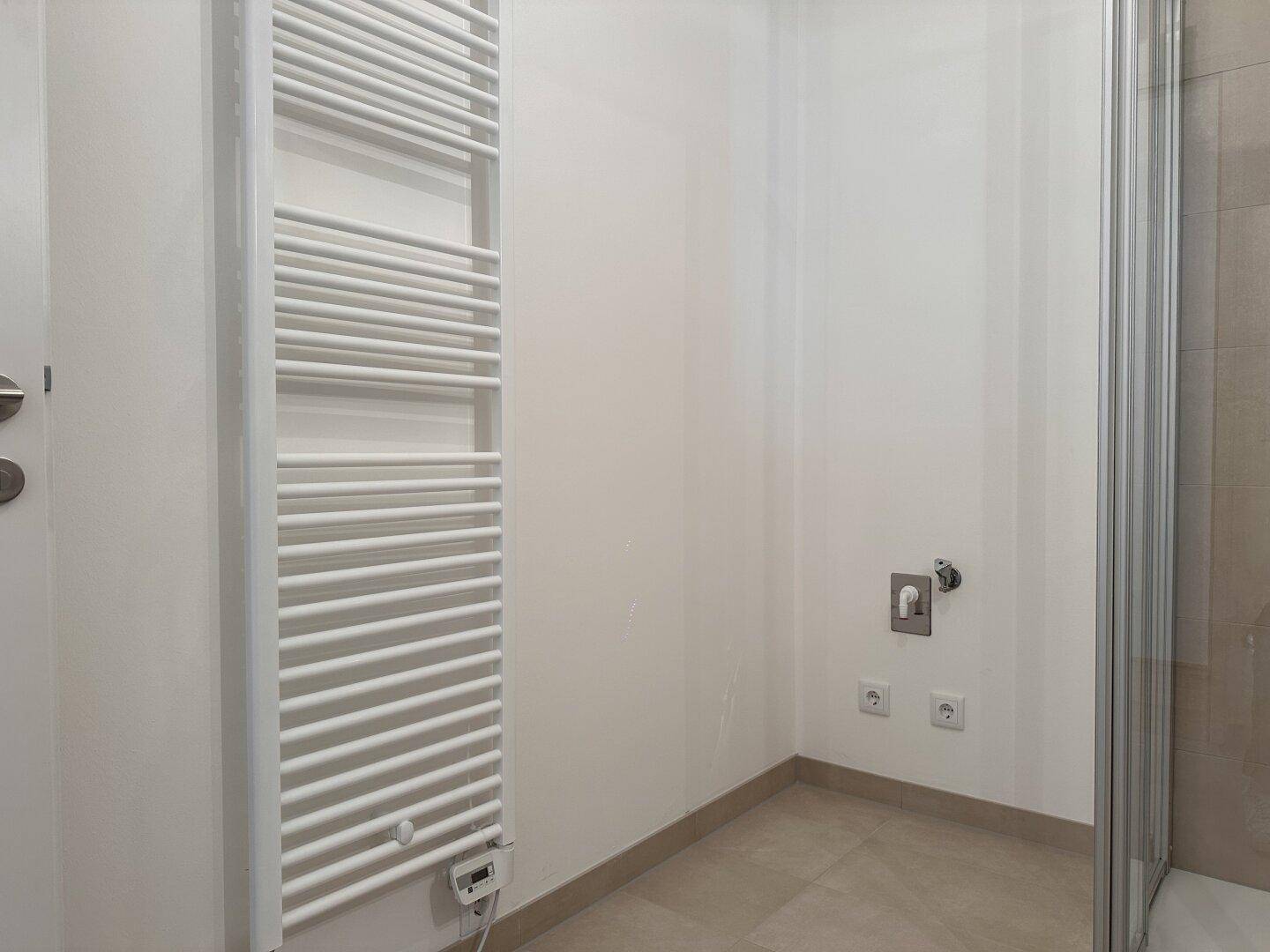 Badezimmer mit Handtuchheizkörper und Anschlüssen für Waschmaschine oder Trockner.
