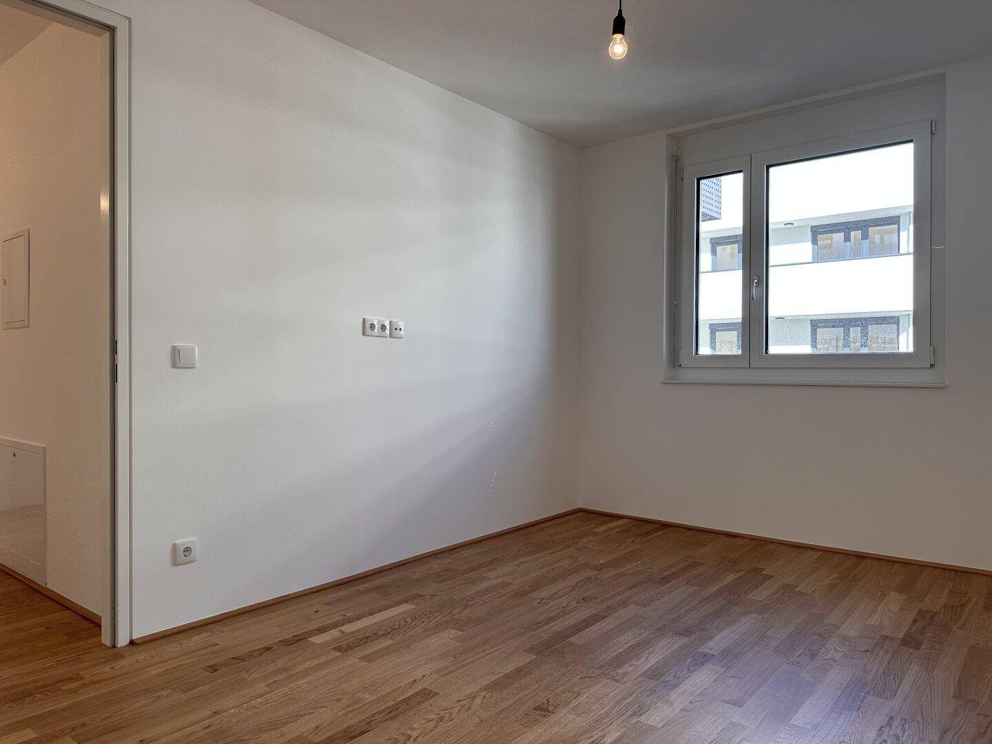 Helles Schlafzimmer mit Parkettboden und großem Fenster, bereit zur Einrichtung.