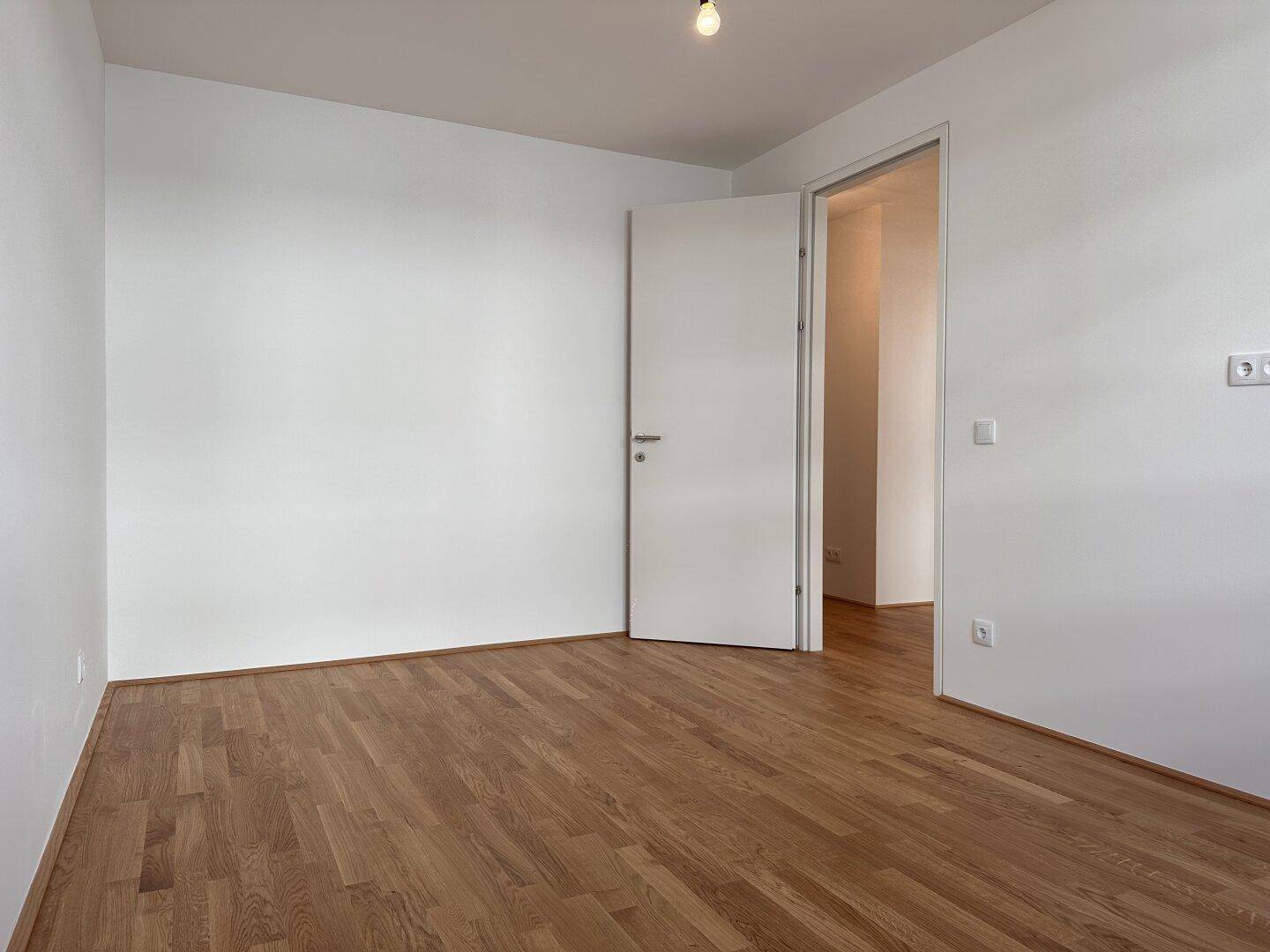 Geräumiges Schlafzimmer mit Parkettboden und Zugang zu einem weiteren Raum.