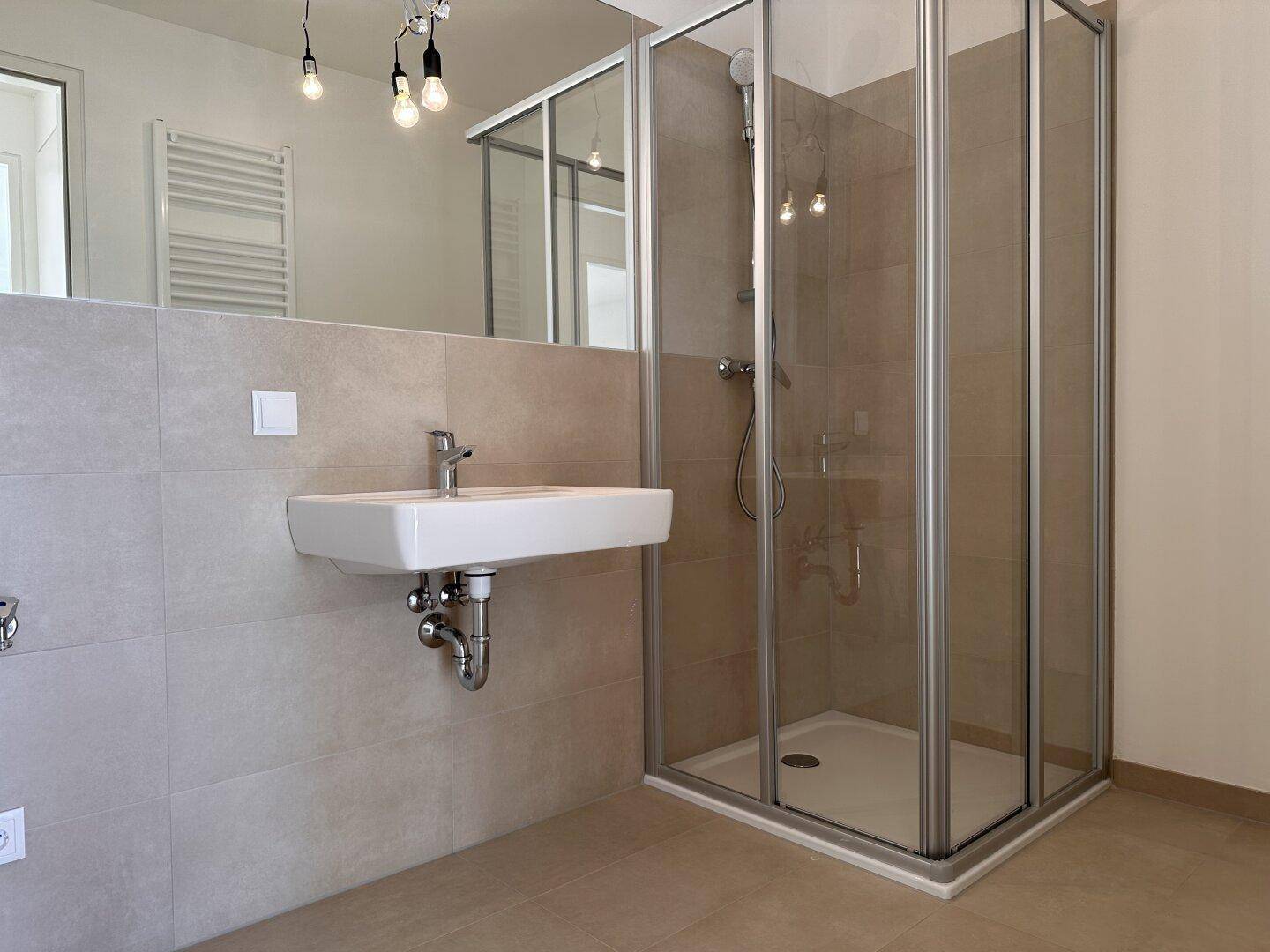 Modernes Badezimmer mit Dusche, Waschbecken und großem Spiegel, in hellen Fliesen gehalten.