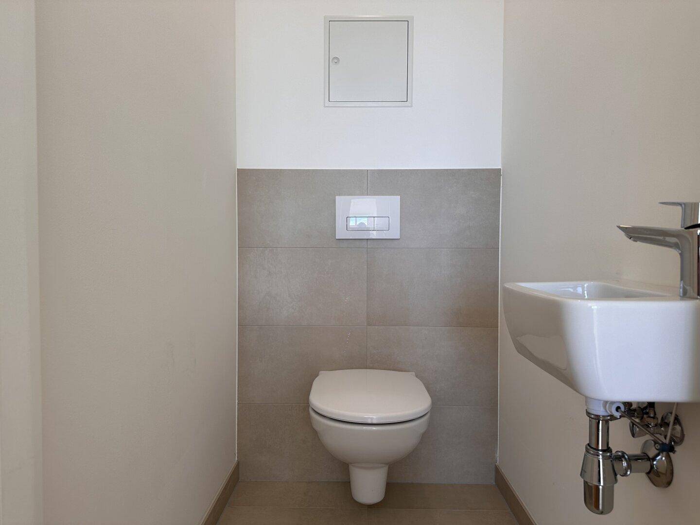 Modernes Gäste-WC mit wandhängender Toilette und kleinem Waschbecken, in hellen Fliesen.