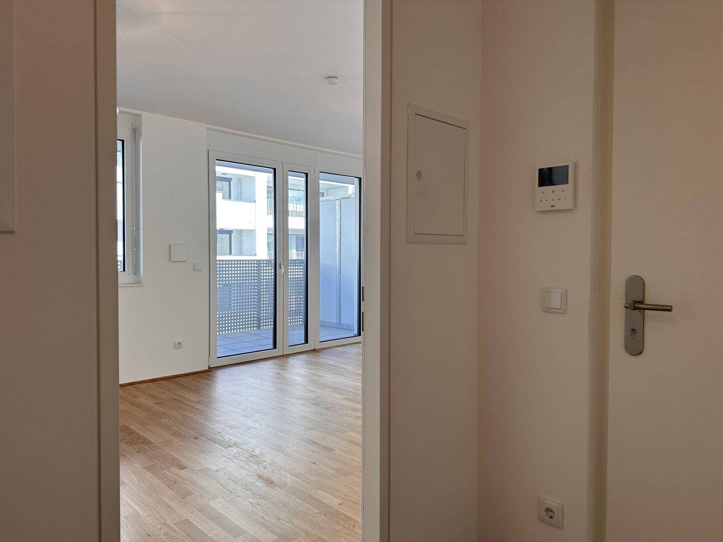 Blick vom Flur in einen hellen Raum mit großen Fenstern und Zugang zu einem Balkon.