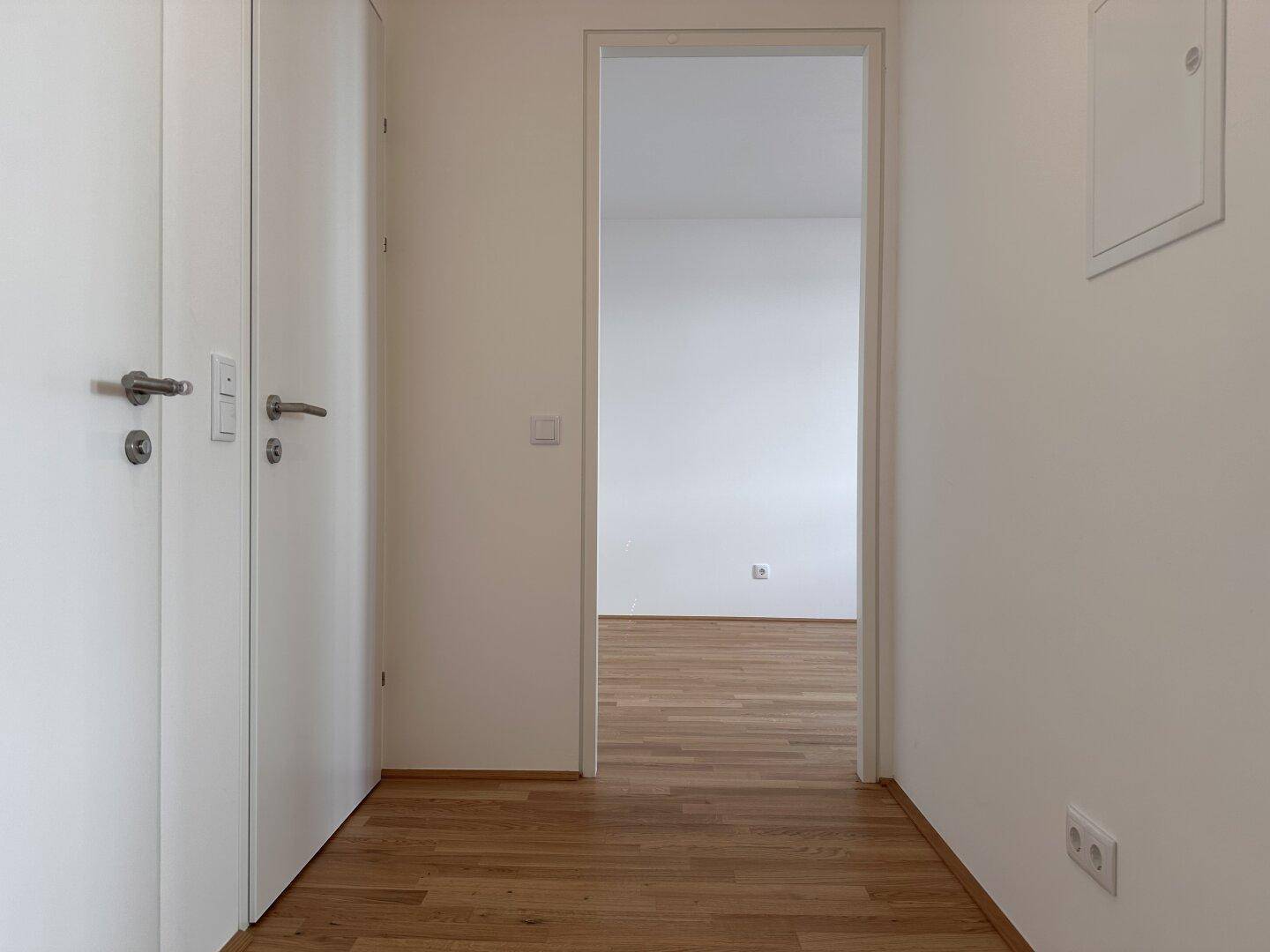 Heller Flur mit weißen Türen und Parkettboden, der zu einem weiteren Zimmer führt.