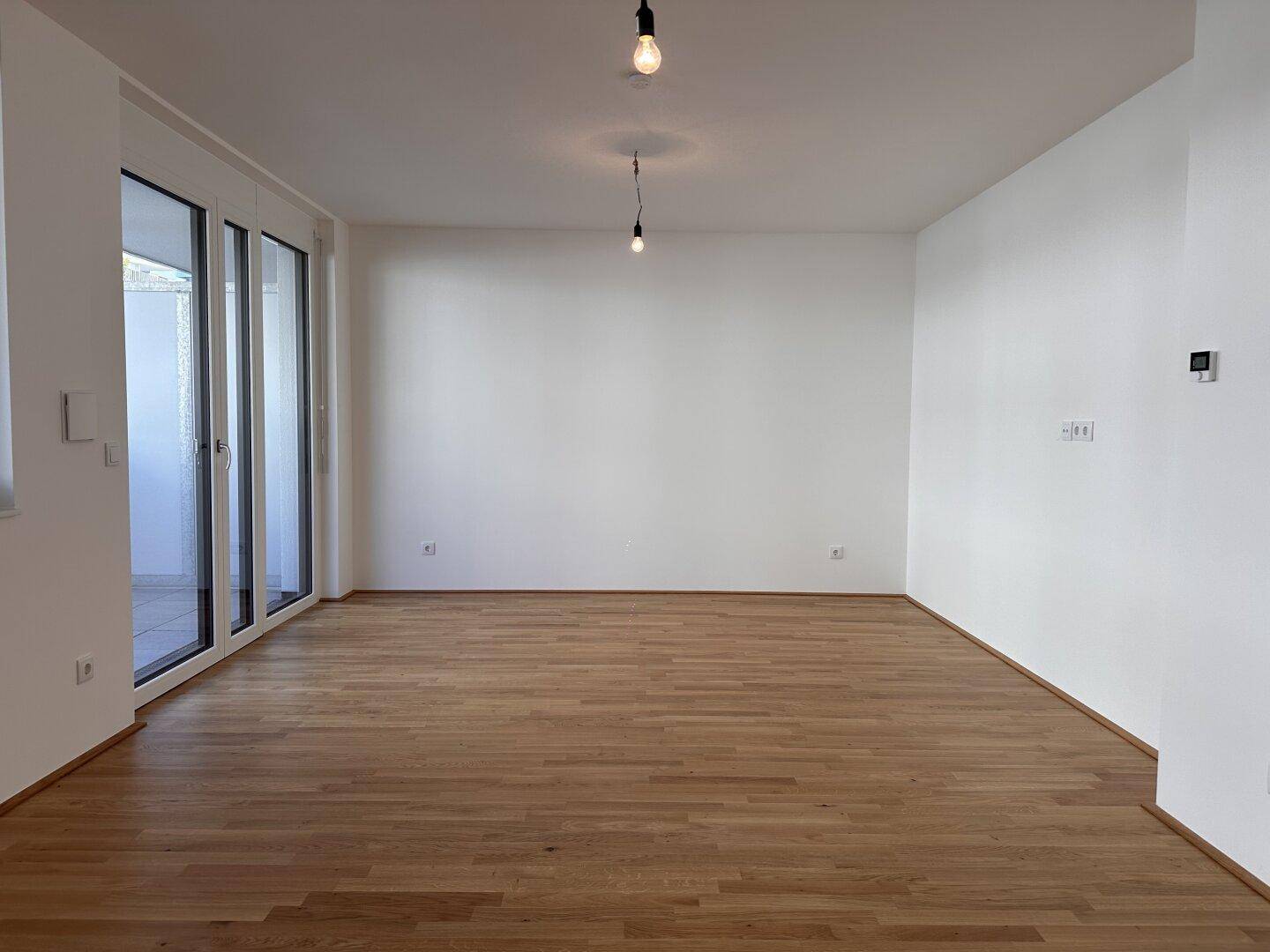 Geräumiges, helles Zimmer mit Parkettboden und Zugang zu einem Balkon, ideal als Wohnbereich.