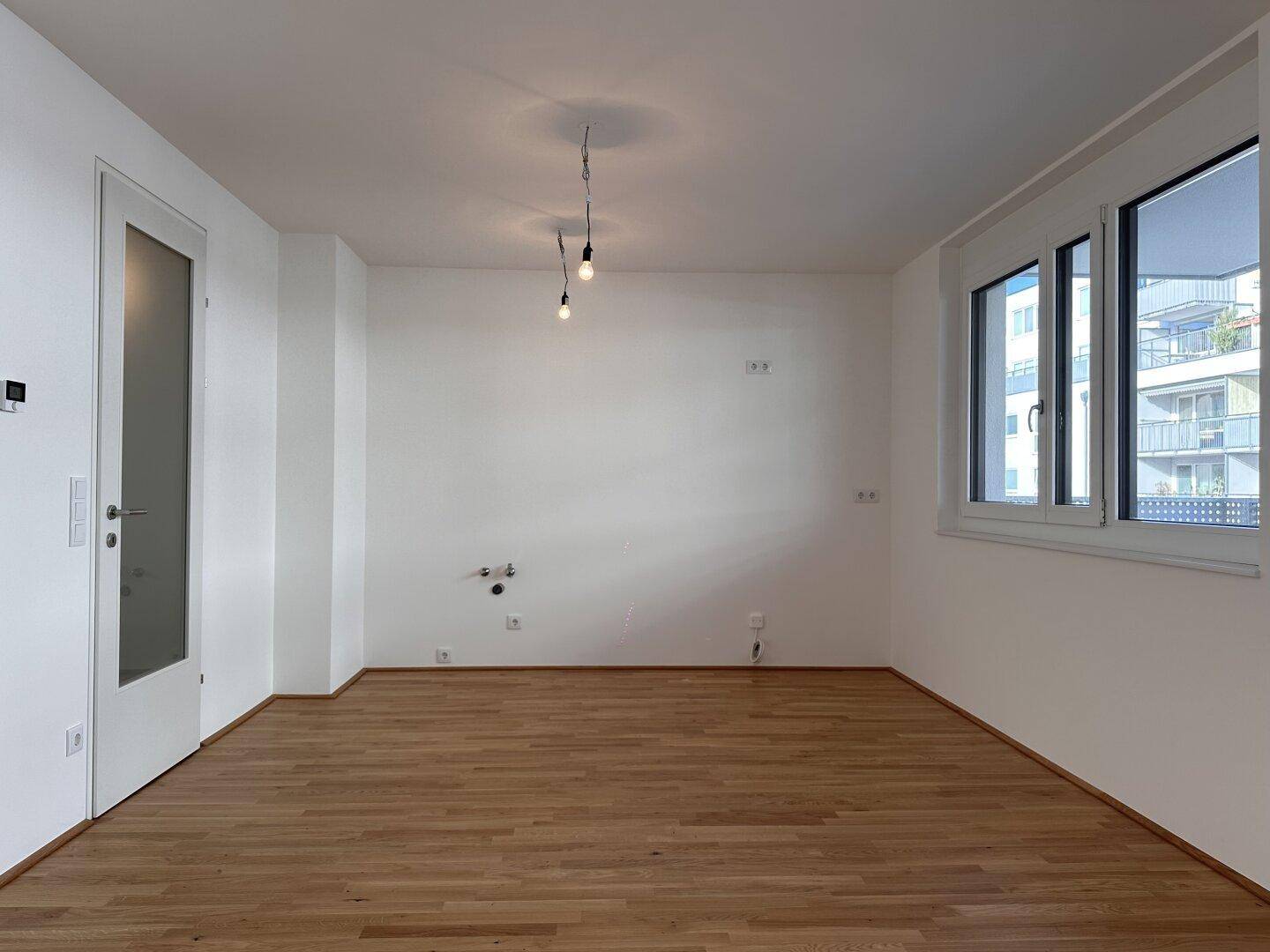 Heller Raum mit Parkettboden und Fenster, vorbereitet für eine moderne Küche mit Anschlüssen.