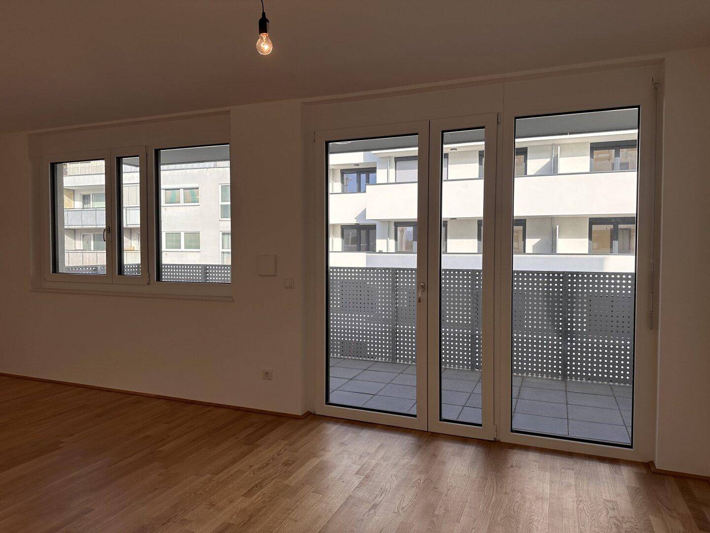 Geräumiges, helles Zimmer mit Parkettboden und breiter Balkontür, die viel Licht hereinlässt.