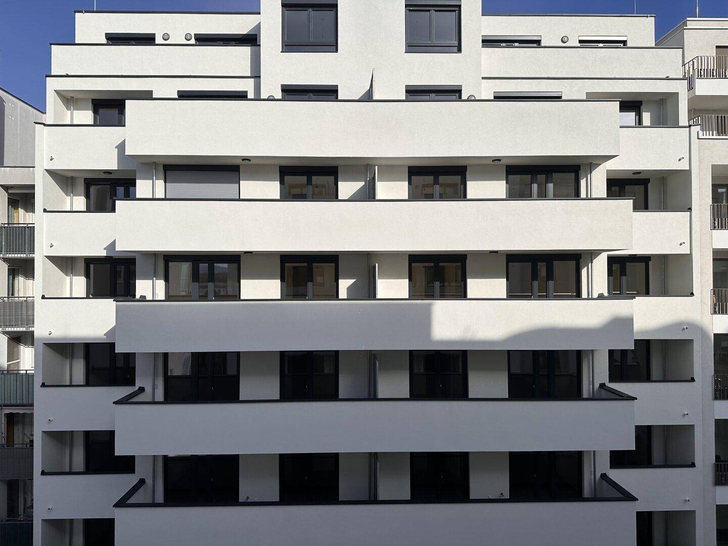 Moderne Fassade eines Apartmentgebäudes mit gestuften Balkonen und großen Fenstern.