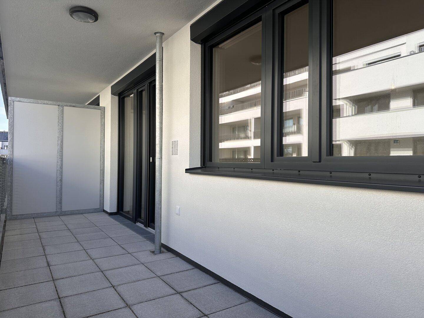 Heller Balkon mit grauen Fliesen und moderner Metallbrüstung, mit Blick auf umliegende Gebäude.