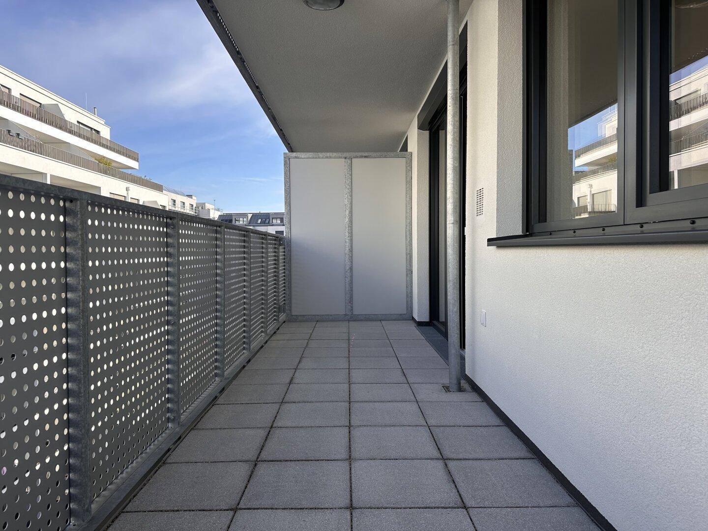 Geräumiger Balkon mit grauen Fliesen und perforierter Metallbrüstung, bietet Platz im Freien.