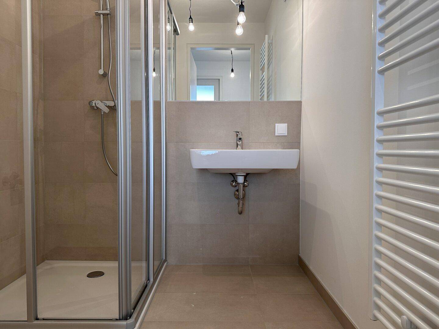 Modernes Badezimmer mit Duschkabine, Einzelwaschbecken, Spiegel und beheiztem Handtuchhalter.